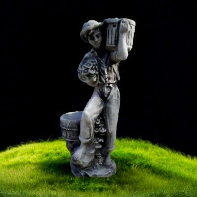 Серая бетонная скульптура мальчика с корзинами стоит на ярко-зелёной траве на чёрном фоне в садовом декоре