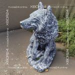 Серо-белая бетонная фигура волка с поднятой головой, стоящая на овальном основании возле садовой зелени